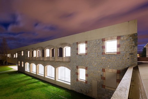 A beautifully illuminated stone hospital with arches under a twilight sky, showcasing architectural