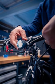 Hand adjusts the light on the bicycle handlebars in a dark blue workshop, technical focus, Waldbike