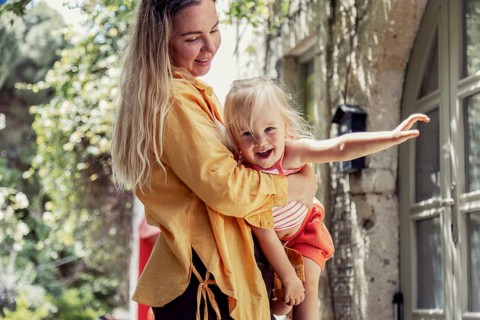 A joyful mother lovingly holds her daughter in an outdoor setting, surrounded by nature. The scene