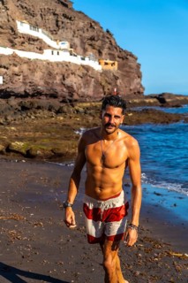 Young hispanic man walking on the beach of tufia, a coastal village of gran canaria, canary