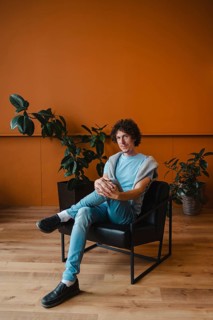 A young man with curly hair sits in a stylish chair in a contemporary room. The space features a