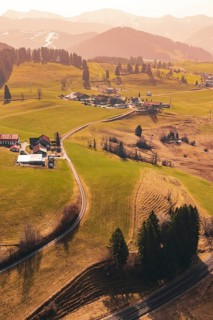 A small village is nestled in rolling hills and green meadows, surrounded by mountains, Oberreute,