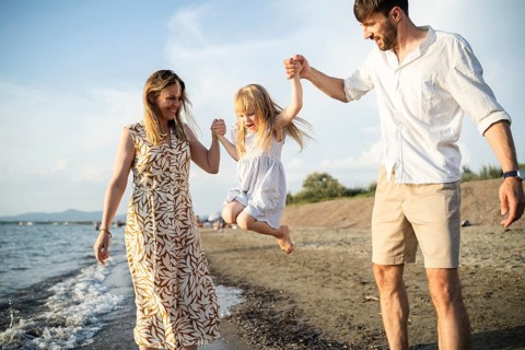 A cheerful family enjoys their time by the sea in Italy, as the parents swing their daughter into