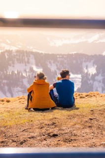 Couple sitting on a mountain peak with a view of the sunny winter valley, Hochgrat Mountains,