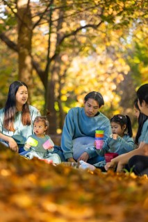 An Asian family enjoying a peaceful picnic surrounded by autumn foliage. They are sitting on a