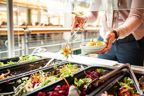Fresh salads in a salad bar, a woman helps herself at the buffet