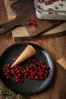 Top view of a rustic food scene featuring red currants on a dark plate beside a waffle cone, set