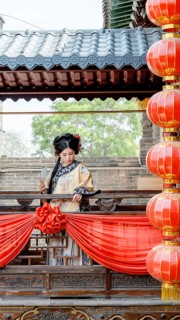 A woman in traditional Qing Dynasty attire stands gracefully on a decorated balcony in Pingyao,