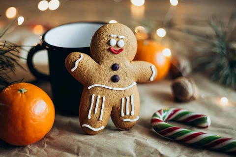 A delightful gingerbread man cookie adorned with icing stands beside a mug, surrounded by festive