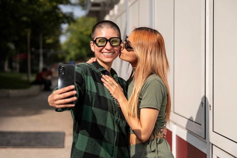 A joyful Colombian lesbian couple takes a selfie outdoors, showcasing their love and happiness.