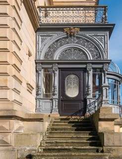 Historic door with filigree decorations and railings on a stone staircase in sunlight, Landau,