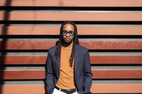 Stylish cuban business man with dreadlocks in sunglasses and casual blazer stands against modern