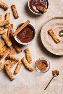 Top view of homemade churros generously dusted with sugar and cinnamon, accompanied by a rich