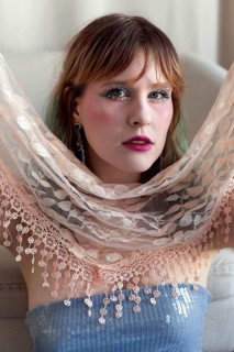 A woman with vibrant makeup and a sequined top poses gracefully, holding a delicate lace shawl Her