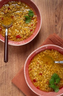Enjoy a hearty grain soup featuring a vibrant mix of ingredients served in two rustic bowls,