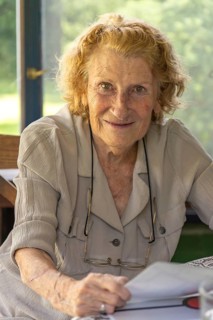 Happy retired woman with curly hair holding a book and smiling, enjoying her leisure time at home,