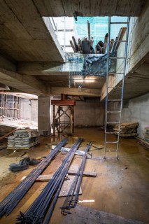 A construction site with steel beams, wooden planks, and a blue ladder. The area is lit naturally,