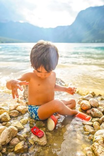 Young child enjoying summer vacation, playing with a toy car by the water's edge of lake bohinj in