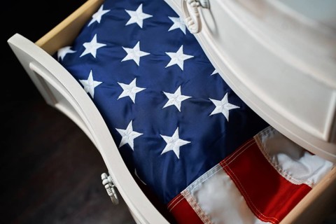 A folded American flag rests neatly inside a white wooden drawer, symbolizing national pride and