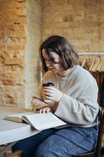 A young woman sits in a charming bookstore, engrossed in a book, while enjoying a hot coffee The