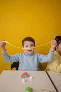 A child joyfully stretches colorful modeling clay during a creative lesson. The bright yellow