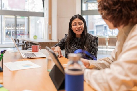 Colleagues discussing a project in a bright office space Laptops, documents, and a coffee mug are