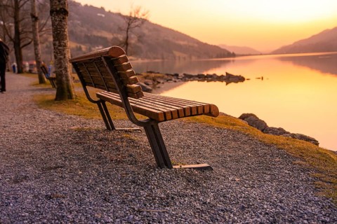 An empty wooden bench on the lakeside at sunset on a gravel path, Großer Alpsee, Immenstadt im