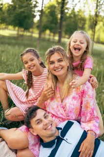 A joyful family shares a happy moment together in a lush green park, laughing and embracing. The
