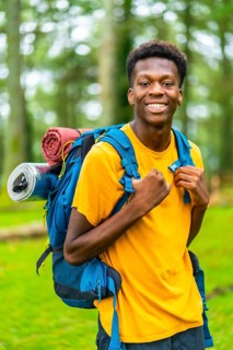 Vertical portrait of a young african man having a walk with a backpack through beautiful nature