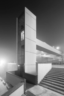 A modern, isolated urban elevator shrouded in thick fog at night captures a both mysterious and