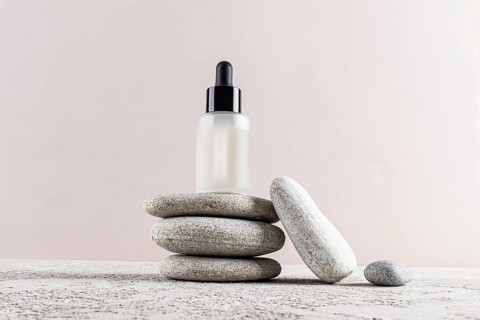A minimalist skincare concept with a frosted glass dropper bottle placed elegantly on a stack of