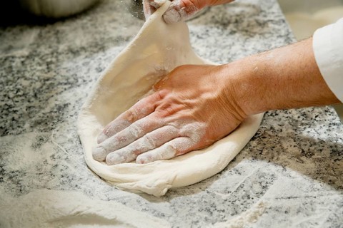 Cropped unrecognizable person kneading fresh pizza dough on a flour-dusted marble countertop,