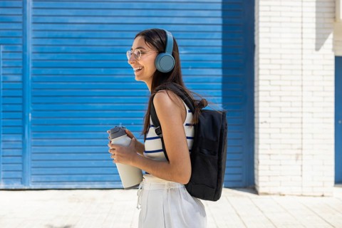 A woman enjoys city life outdoors, wearing headphones and carrying a water bottle, embodying an