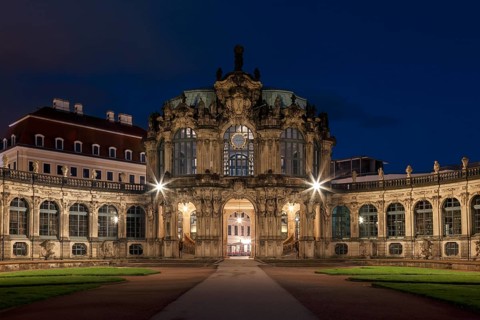The Zwinger Palace in Dresden, Germany, is beautifully illuminated under a deep blue night sky.