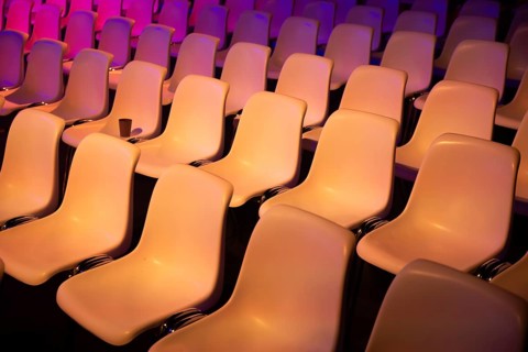 Rows of empty seats at a conference of AI in Amsterdam by vibrant purple and orange lights. The