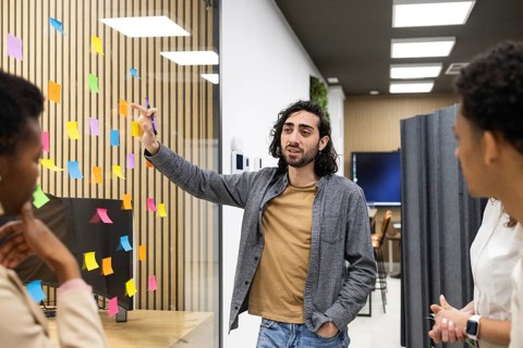 Professionals engage in a brainstorming session in a modern office space. A man gestures towards