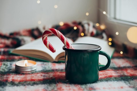 Cozy Christmas setting featuring a green mug, a festive candy cane, and a flickering candle next to