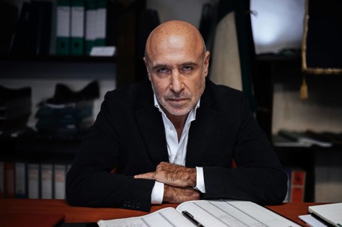 Portrait of a confident businessman seated at a desk, surrounded by office files. The scene conveys