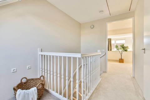 A modern, bright interior hallway features a white railing and plush carpet, accented by a wicker