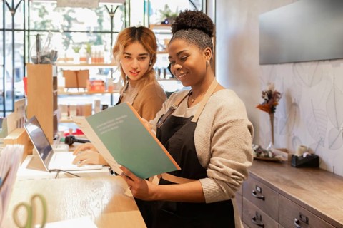 Two workers in a cosmetics store engage in tasks at the counter. One reads a catalog while the