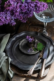 A rustic table setting features antique pewter plates and cutlery, adorned with vibrant lilac