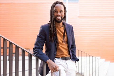 Cuban business man with long hair wearing a blazer and casual attire, leaning against a staircase