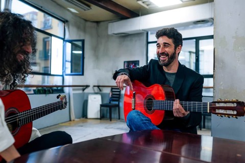 Male friends playing guitars at table in music studio