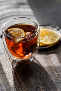 A warm glass of English tea, infused with a slice of lemon, presented on a rustic wooden table,