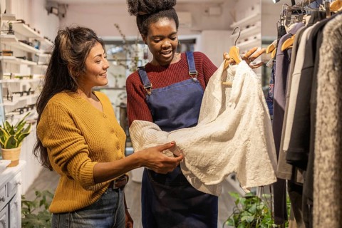 A boutique employee assists a customer in choosing clothing. They are smiling and engaged while