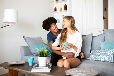 A couple sits together on a comfortable couch, sharing a warm moment with coffee. The bright and