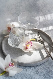 A refined dining setup featuring ribbed glassware, delicate orchids, and sleek cutlery on a