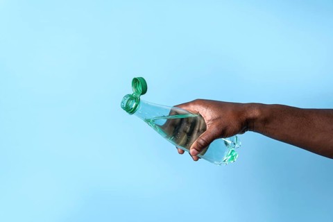 A close-up image of a hand holding a transparent water bottle with a green cap, set against a