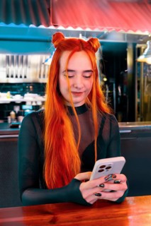 A young woman with vibrant red hair checks her phone in a lively market ambiance, blending modern