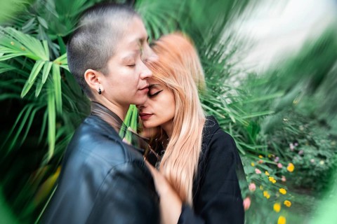 A lesbian couple shares a tender, intimate moment surrounded by vibrant greenery, symbolizing love
